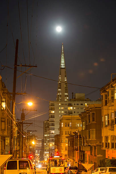 San Francisco, CA, USA - November 14, 2016: Transamerica Pyramid and supermoon on the background.Cable car rail in the front and pass through Washington Street. One cable car on the background. Some cars parked on the sides. 