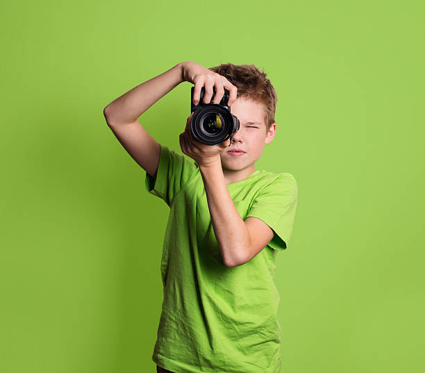 Photographer. Teenage boy using professional camera, isolated on green background.