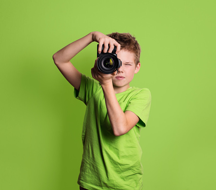 Photographer. Teenage boy using professional camera, isolated on green background.