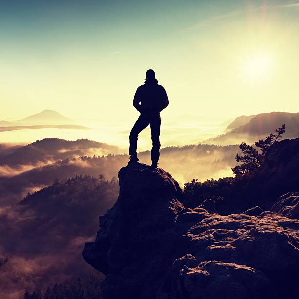 istock Man silhouette stay on sharp rock peak. Hiker enjoy view. 628276204