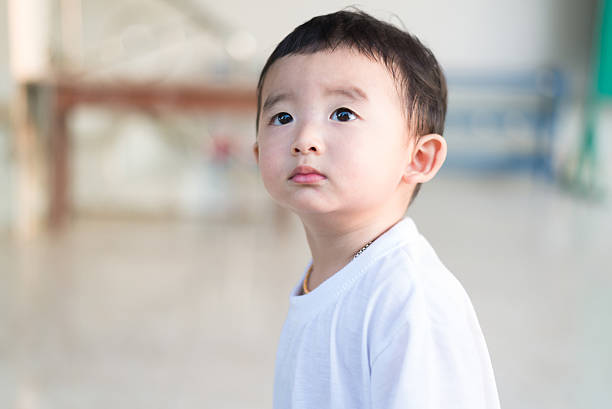 Close-up little Asian boy in white t-shirt looking up somewhere and thinking with some hope, shallow DOF.