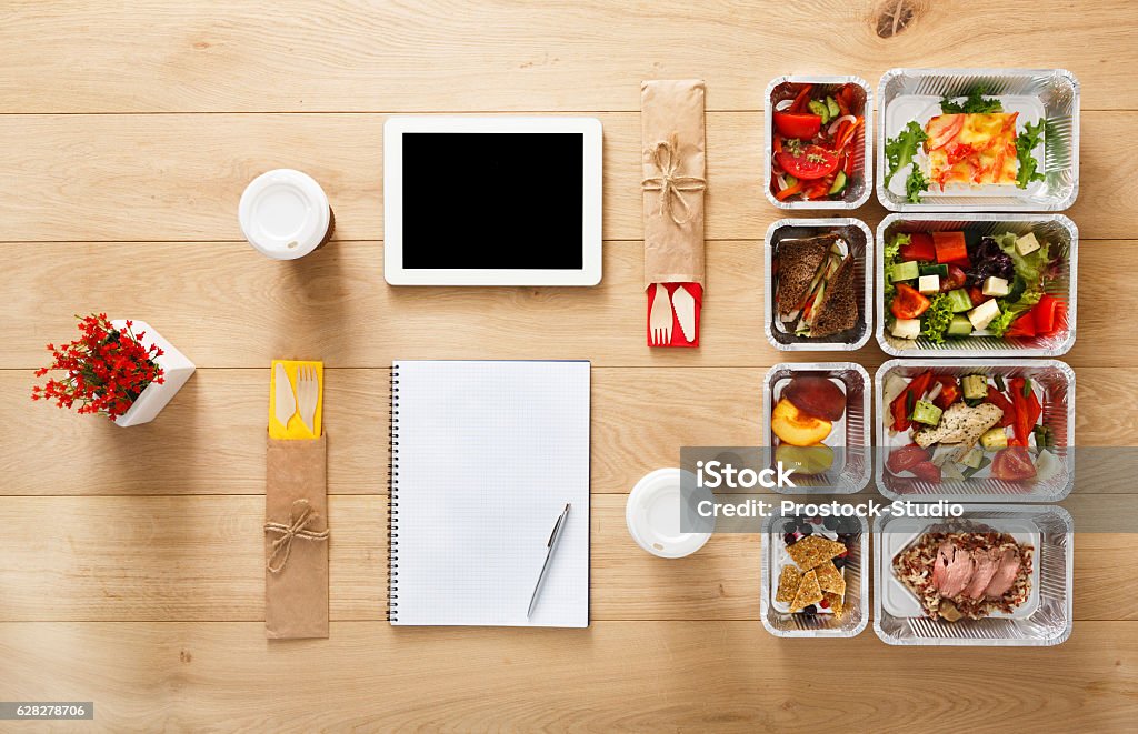 Healthy food take away in boxes, top view at wood Healthy restaurant food for couple and diet plan. Fresh daily meals delivery. Fitness nutrition, vegetable, meat and fruits in foil boxes, coffee and tablet. Top view, flat lay on wood with copy space Meal Stock Photo