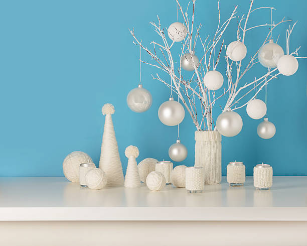 Vase in white knitted cover with white branches and Christmas toys. Candle holders in knitted covers with candles. Christmas tree made from white yarn.