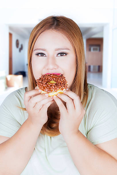 istock Overweight woman eats donut at home 628280446