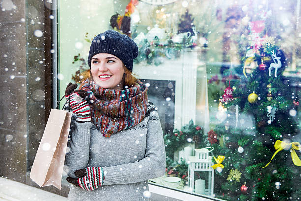 A girl stands at the storefront decorated with Christmas lights. A girl holding a bag with gifts. Happy woman, winter, snow. Copy space.
