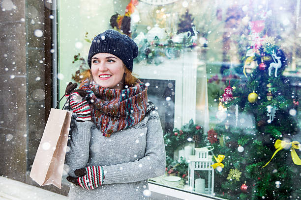 girl holding a bag with gifts A girl stands at the storefront decorated with Christmas lights. A girl holding a bag with gifts. Happy woman, winter, snow. Copy space. holiday shopping stock pictures, royalty-free photos & images