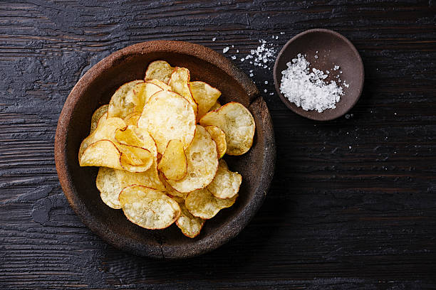Potato chips and ​​salt Homemade crispy Potato chips and sea ​​salt on dark wooden background potato chip photos stock pictures, royalty-free photos & images