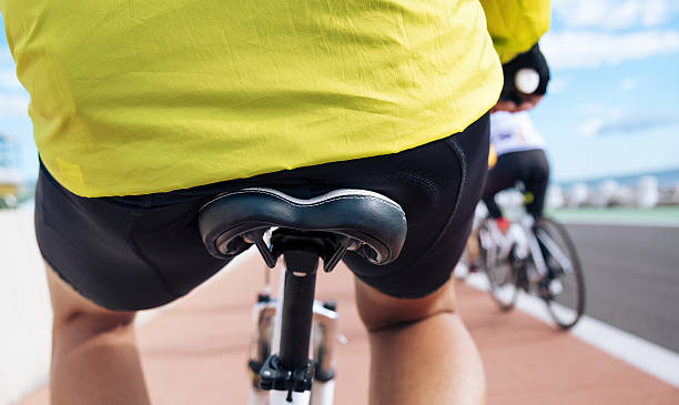 young sportsman riding his bicycle closeup of a young caucasian man wearing sport clothes seen from behind riding his bicycle by a bike lane next to the ocean saddle photos stock pictures, royalty-free photos & images