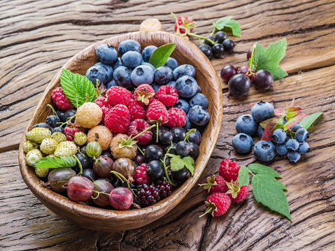 Ripe berries in the wooden bowl on the table.