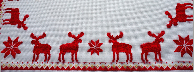 Cross-Stitched red deer on the white tablecloth. Christmas background