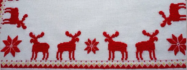 Photo of Cross-Stitched red deer on the white tablecloth. Christmas background