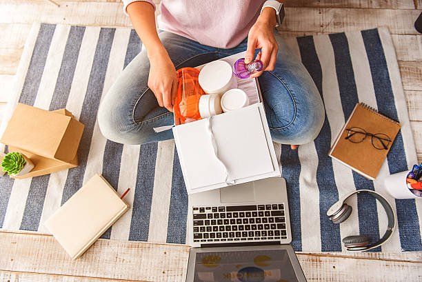 Girl selling cosmetic products through online Top view close-up of young woman hands taking perfume from cosmetology gift box. She is sitting on floor near laptop at home woman legs open stock pictures, royalty-free photos & images