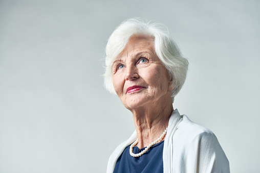 Portrait of elegant-looking elderly woman with smile on face looking upwards against white background
