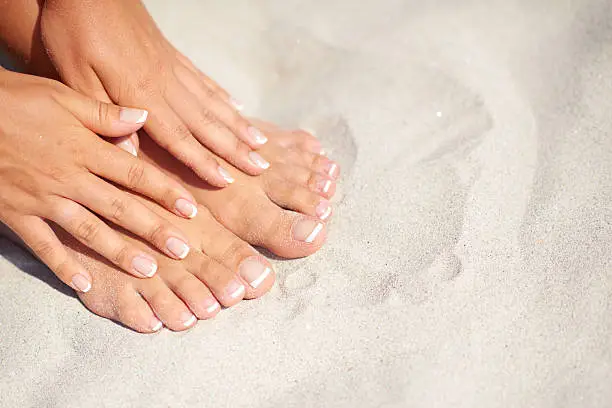 Shoot of manicure and pedicure over sand background on the beach