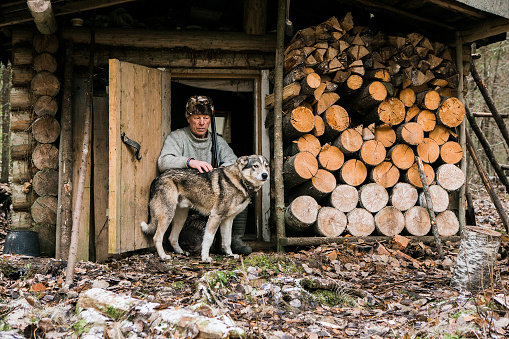 Hunter sits near a hunting lodge with his dog,  forest