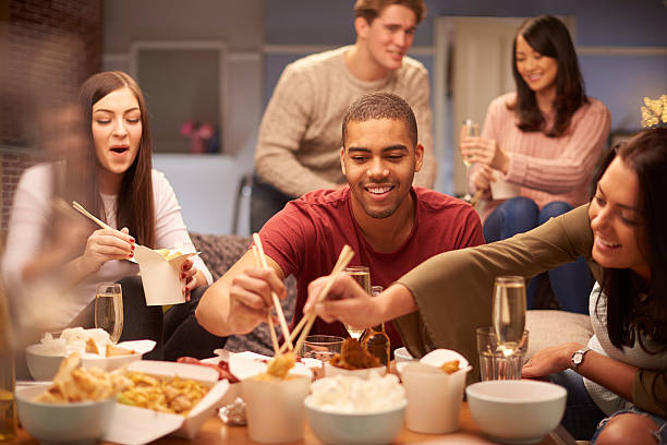 hungry house a group of young friends sit on the sofa and share a chinese take away meal , chatting and laughing with each other as they use their chopsticks to eat . chinese takeout stock pictures, royalty-free photos & images