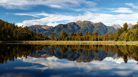 Panoramic of Lake Matheson on New Zealand's South Island, with the Southern Alps reflected in its almost mirror-like surface.