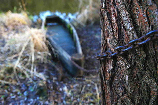 Aged wooden boat tied chain on the shore of the pond