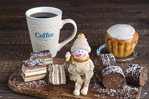 Variety of cakes dusted with powdered sugar, a toy Snowman and coffee mug with the inscription on the wooden surface.