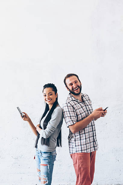istock Cheerful couple standing back to back and using smart phone 628347234