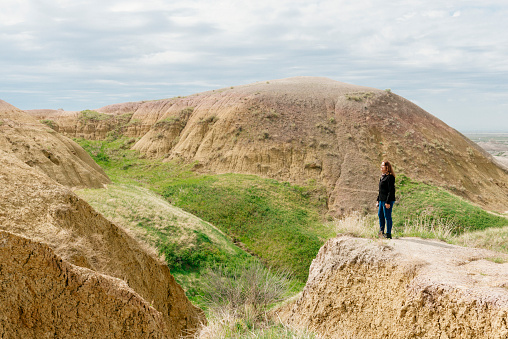 Traveling senior American woman of Hispanic descent stands on the edge of a mountain ridge in Badlands National Park South Dakota and enjoys viewing the beautiful landscape.