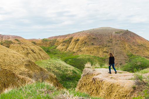 Traveling senior American woman of Hispanic descent walking toward the edge of a mountain ridge in Badlands National Park South Dakota to see the viewpoint of the beautiful landscape. Photographed in spring with a Nikon D800 DSLR camera.