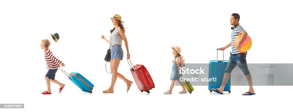 heading for the sun a young family march across the shot pulling their suitcases as they look like they're heading for the airport , or hotel. the little boy at the front is rushing so much his hat has blown off . The family consists of mum , dad, daughter and son . Family Stock Photo