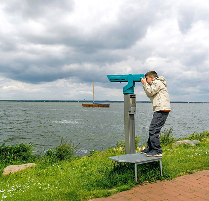 Boy looking through coin-operated binoculars at lake.