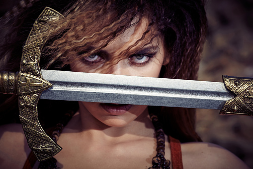 Beautiful girl in the clothes of a Viking or Amazon, with a sword on a background of stones. Closeup portrait.
