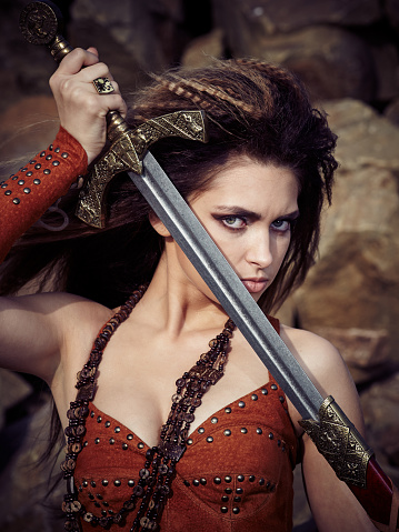 Beautiful girl in the clothes of a Viking or Amazon, with a sword on a background of stones.
