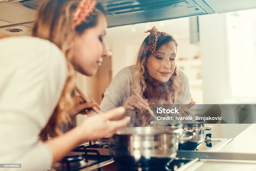 Young woman cooking in the kitchen Young women cooking and testing the food in the kitchen. Smelling Stock Photo