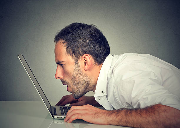 man with vision problems using computer reading email Side profile young man with vision problems using computer reading email browsing internet squint eyes stock pictures, royalty-free photos & images