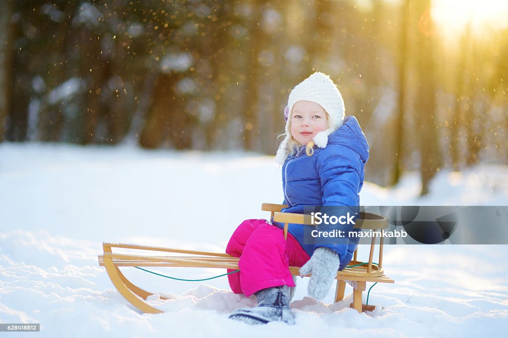 Funny little girl having fun with sleigh in winter park Funny little girl having fun with a sleight in beautiful winter park Child Stock Photo