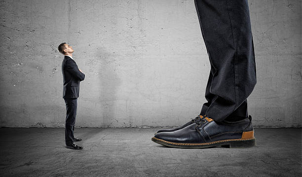 Tiny businessman looking up on huge legs of another man Tiny businessman looking up on huge legs of another businessman. Career growth and opportunities. Confident behaviour. small stock pictures, royalty-free photos & images