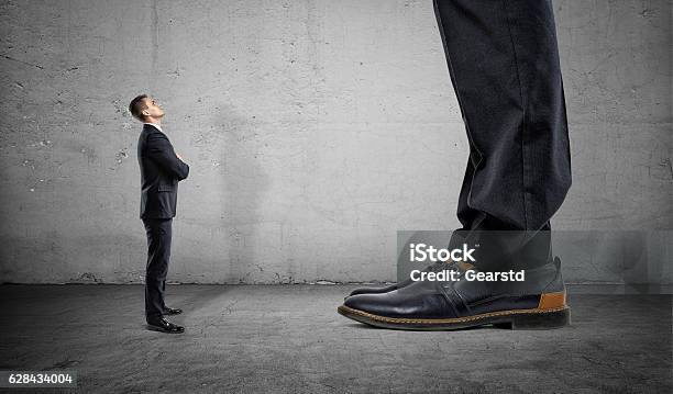 Tiny Businessman Looking Up On Huge Legs Of Another Man-foton och fler bilder på Stor