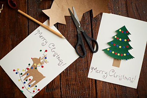 Handmade Christmas cards, scissors and pencil on wooden table