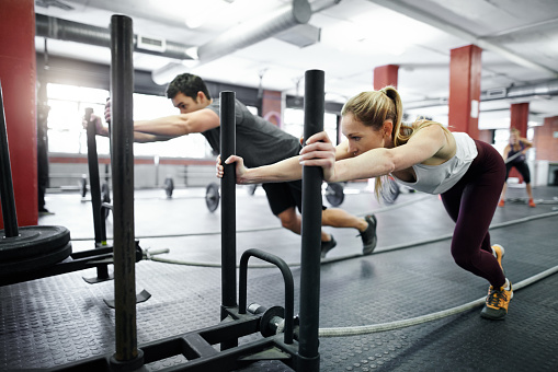 Shot of two people pushing weight sleds in a gym