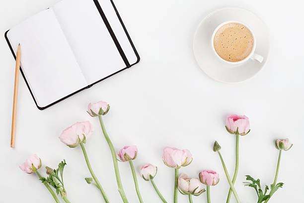 Ranunculus flowers, empty notebook and cup of coffee. Flat lay.