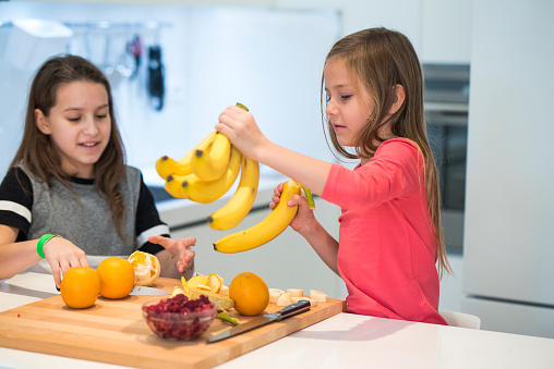 Two little girls preparing fruit smoothie in the kitchen