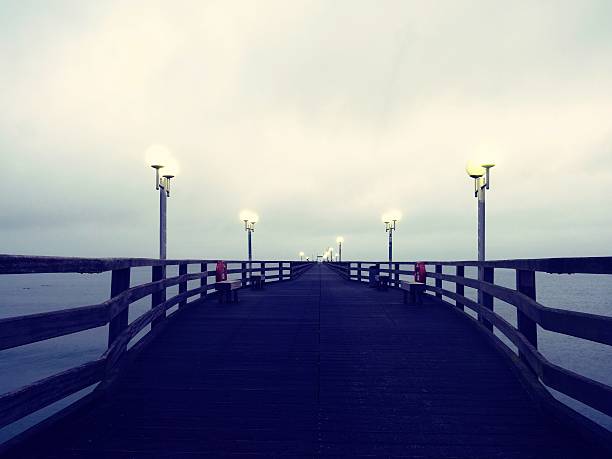 istock Pier at misty night with yellow lights on dark background 628463674