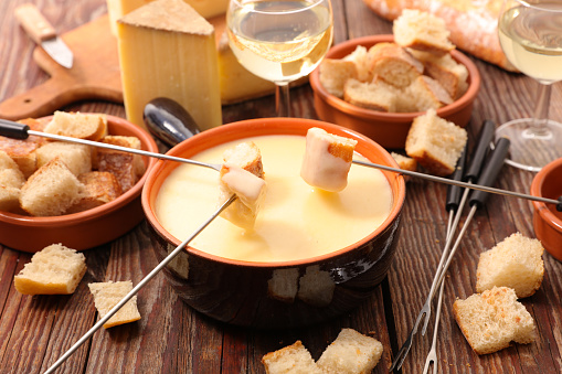 Delicious fondue cheese with bread slices and white wine. On a wooden background.
