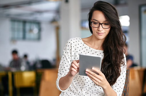 Shot of a young woman using a digital tablet while sitting in a modern office