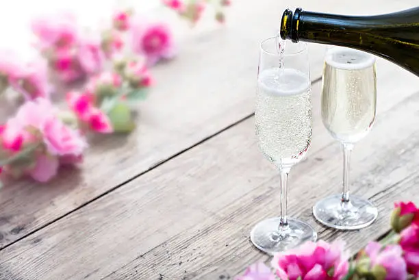 Prosecco poured into a glass. Spring or Summertime, outdoors on rustic garden picnic table with flowers in background.