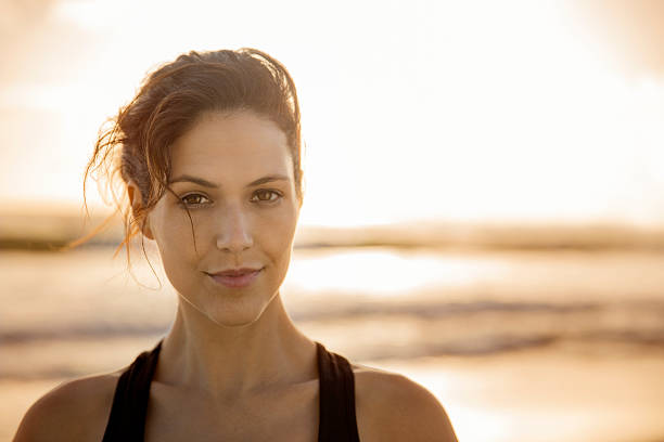 selbstbewusste junge frau am strand bei sonnenuntergang - healthy lifestyle women beach looking at camera stock-fotos und bilder