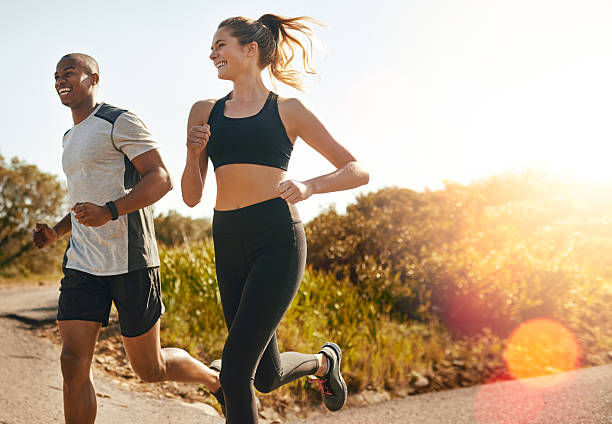 They keep each other going Shot of a fit young couple going for a run outdoors sportswear stock pictures, royalty-free photos & images