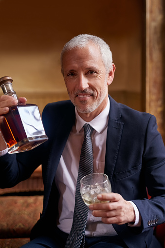 Portrait of a well-dressed mature man holding a glass and whiskey bottle in a bar after work