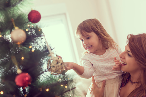 Mother and daughter decorating Christmas tree and having fun. Focus on the daughter