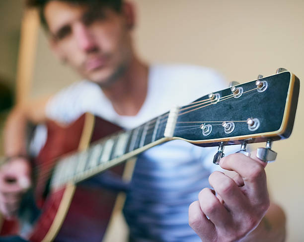 Playing in tune Shot of a handsome young man playing guitar at home tuning guitar stock pictures, royalty-free photos & images