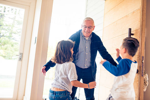 Children running towards their grandfather that just came through front door of their house. One little girl and one little boy. They are happy, smiling.