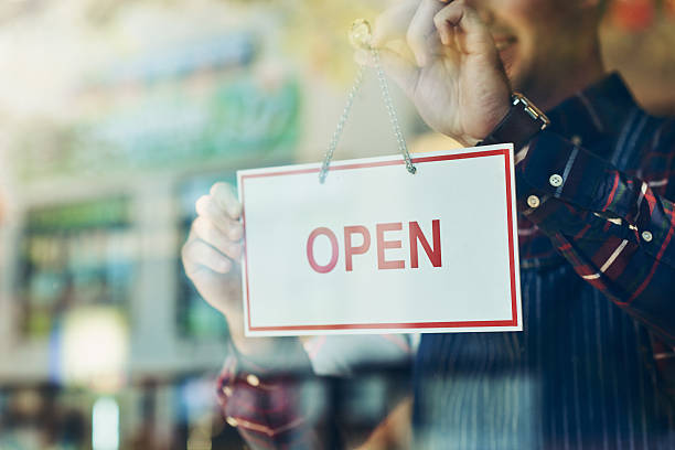 Opening day has arrived Closeup shot of a young man hanging up an open sign in a shop window franchising photos stock pictures, royalty-free photos & images
